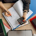 Een ondernemer die aan een bureau werkt en zakelijke facturen en uitgaven beheert, met een calculator en notities.